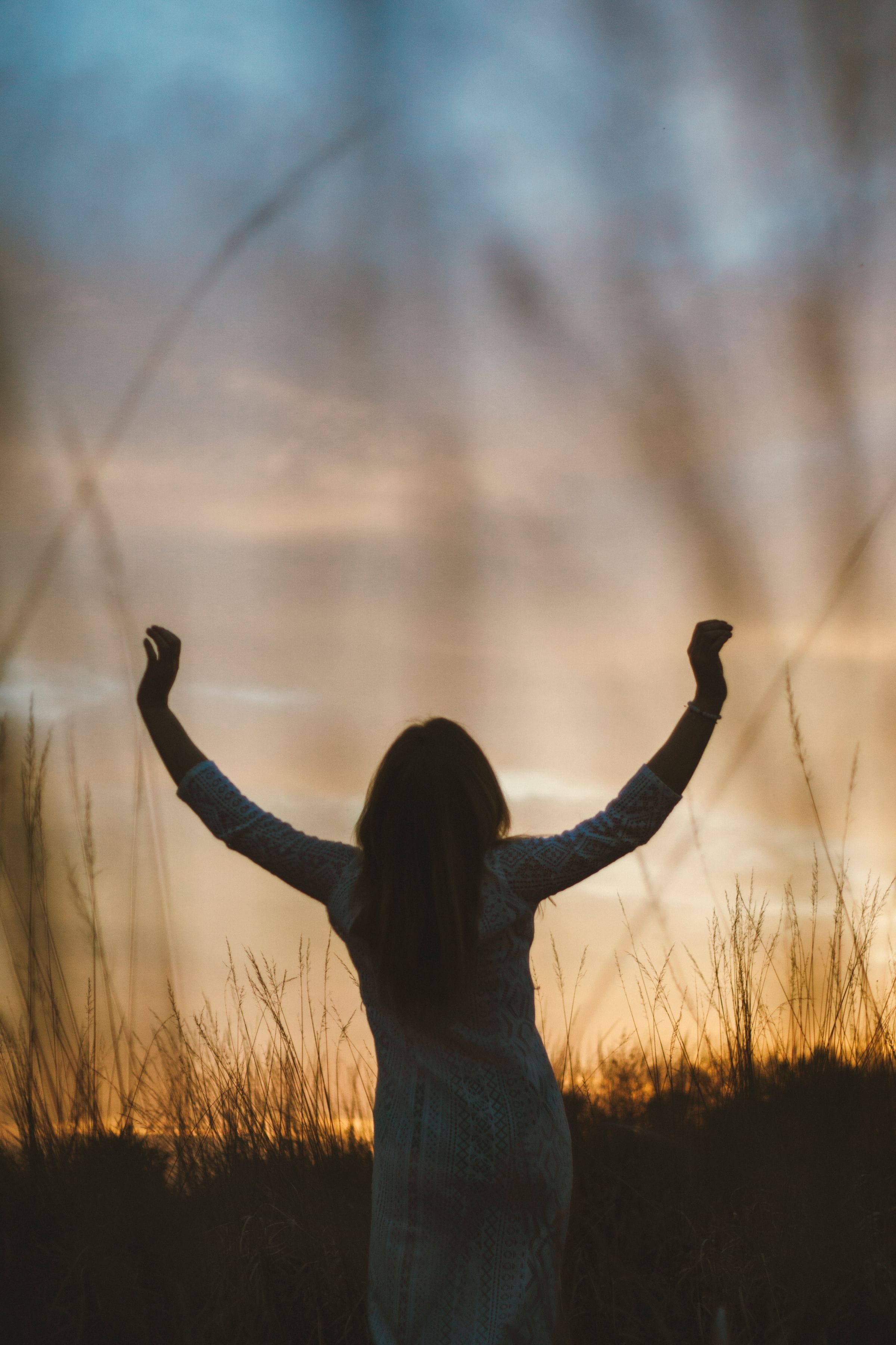 Personne debout dans un champ au coucher du soleil, les bras ouverts vers le ciel